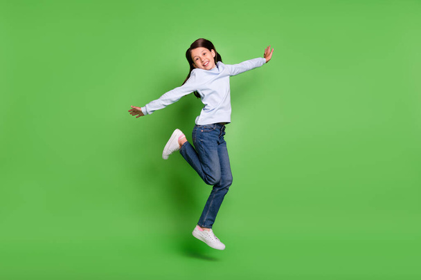 Photo of cute beautiful schoolgirl wear blue turtleneck jumping high arms sides smiling isolated green color background - Fotoğraf, Görsel