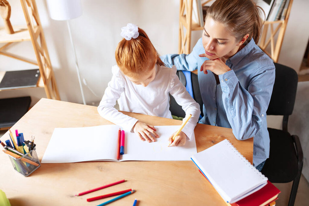 Top view image of mother helping her daughter with homework, doing drawings - Photo, image
