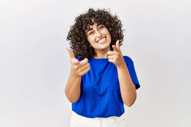 Mladá žena ze Středního východu, stojící nad izolovaným pozadím a ukazující prstem na kameru se šťastnou a zábavnou tváří. dobrá energie a vibrace.  - Fotografie, Obrázek