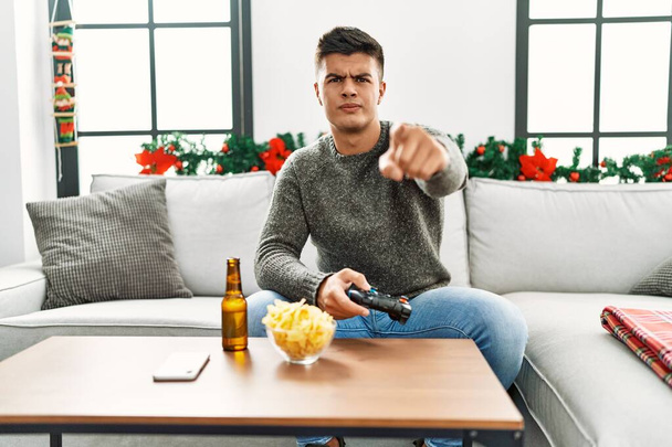 Молодий іспаномовний чоловік грає в відеогру на Різдво, вказуючи пальцем на камеру і до вас, впевнений жест виглядає серйозно
  - Фото, зображення