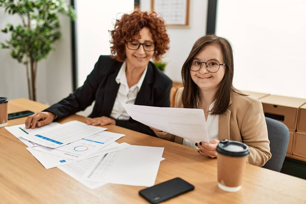 Group of two women working at the office. Mature woman and down syndrome girl working at inclusive teamwork. - Photo, Image