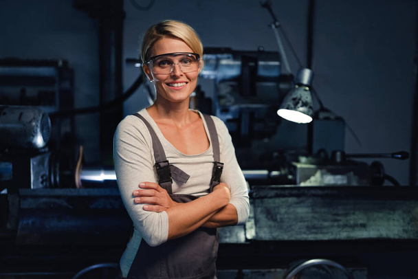 Portrait of mid adult industrial woman working indoors in metal workshop, looking at camera. - Photo, image