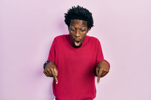 Nuori afrikkalainen amerikkalainen mies yllään rento vaatteita alaspäin sormilla osoittaa mainos, yllättynyt kasvot ja avoin suu  - Valokuva, kuva