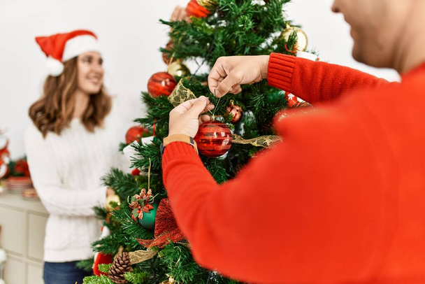 Young hispanic couple decorating christmas tree at home. - Foto, imagen