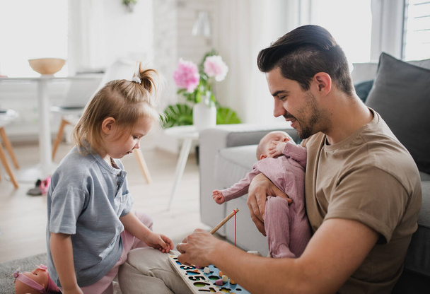 Happy young man taking care of his newborn baby and little daughter indoors at home, paternity leave - Photo, Image