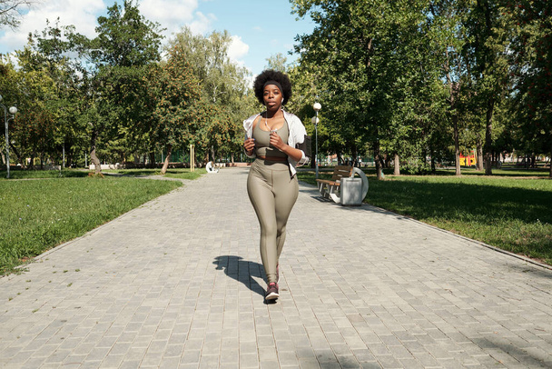 Młody aktywny plus rozmiar kobieta jogging wzdłuż drogi - Zdjęcie, obraz