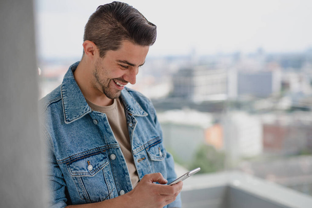Portrait of young caucasian man with smartphone standing on balcony. - Zdjęcie, obraz