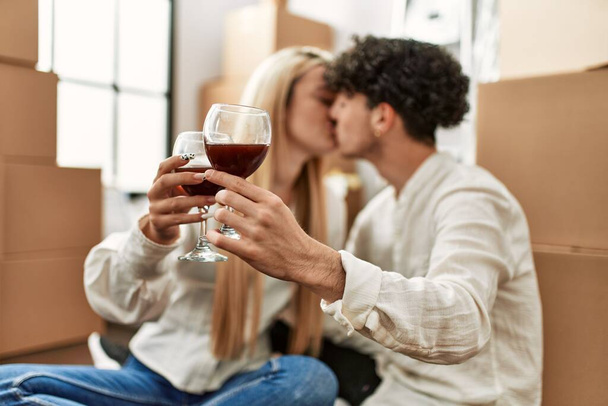 Νεαρό όμορφο ζευγάρι φιλιά και πρόποση με κόκκινο κρασί στο νέο σπίτι - Φωτογραφία, εικόνα