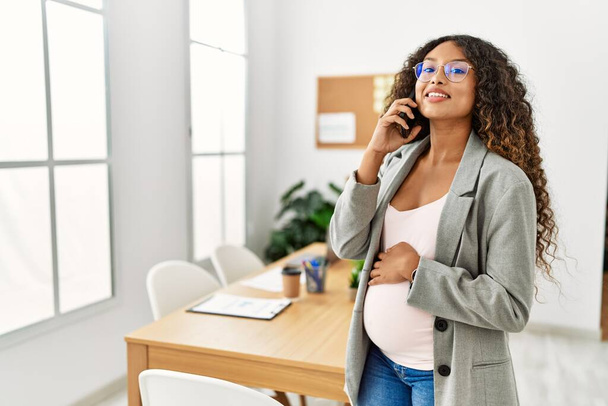 Молода латинка вагітна усміхнена впевнена розмова на смартфоні, що працює в офісі
 - Фото, зображення