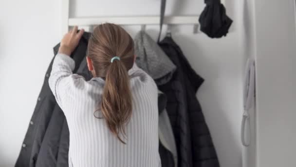 μια νοικοκυρά κρεμάει προσεκτικά εξωτερικά ρούχα της σε άγκιστρα στην είσοδο του διαμερίσματος. - Πλάνα, βίντεο