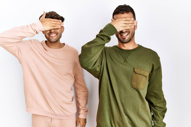 Young gay couple standing over isolated white background smiling and laughing with hand on face covering eyes for surprise. blind concept.  - Fotó, kép