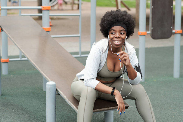 Молода усміхнена спортсменка з навушниками, що спілкуються за допомогою мобільних технологій
 - Фото, зображення