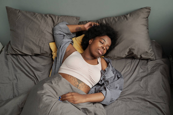 Young tired African woman sleeping in double bed - Φωτογραφία, εικόνα