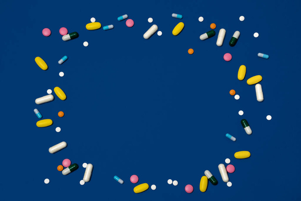 Fondo azul con espacio de copia y muchos medicamentos en cápsulas y tabletas de diferentes colores dispersos en la superficie - Foto, imagen