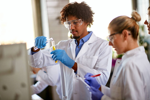 Young students mixing chemicals in a test tube and taking notes about a chemical reaction in a sterile environment of the laboratory. Science, chemicals, lab, people - Photo, image
