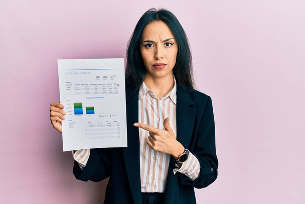 Young hispanic girl wearing business jacket holding document skeptic and nervous, frowning upset because of problem. negative person.  - Foto, afbeelding