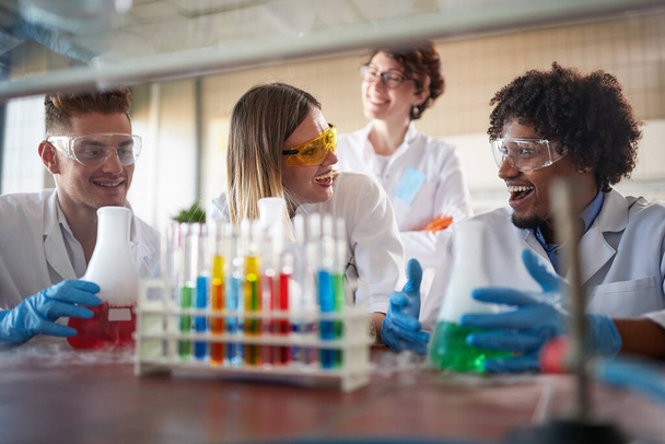 Young chemistry students having a good time in a sterile laboratory environment while working with colorful chemical. Science, chemistry, lab, people - Foto, afbeelding