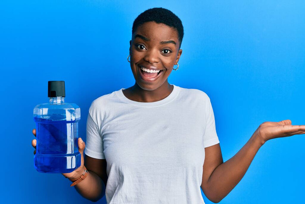 Jeune femme afro-américaine tenant un bain de bouche pour une haleine fraîche célébrant la réalisation avec un sourire heureux et l'expression gagnante avec la main levée  - Photo, image