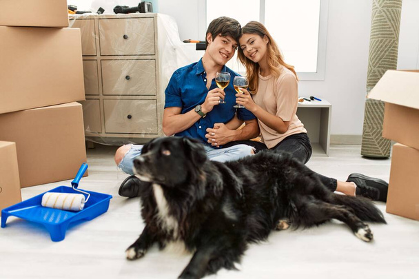 若いですcaucasianカップルトーストとともにシャンパンで床に座って犬とともに新しい家. - 写真・画像