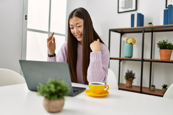 Nuori kiinalainen tyttö, jolla on videopuhelu kannettavan tietokoneen avulla istuu pöydällä kotona. - Valokuva, kuva