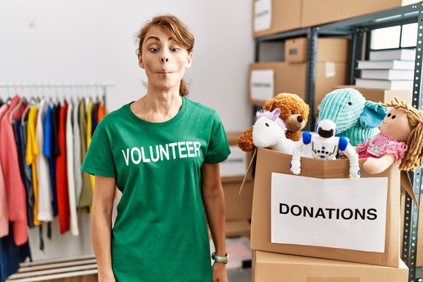 Beautiful caucasian woman wearing volunteer t shirt at donations stand making fish face with lips, crazy and comical gesture. funny expression.  - Photo, Image