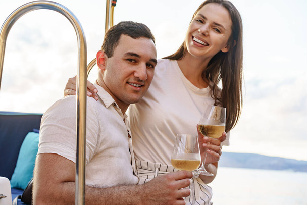 Young loving couple sitting on the yacht deck and drinking wine - Photo, image