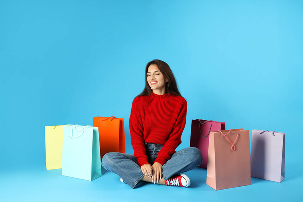 Girl with multicolored paper bags on blue background. - 写真・画像