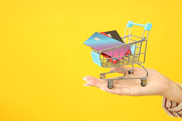 Carro de mano femenino con tarjetas de crédito sobre fondo amarillo. - Foto, Imagen