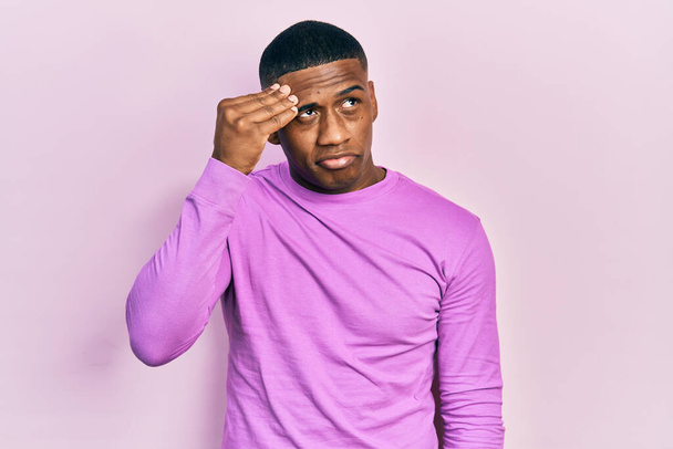 Junger schwarzer Mann in lässigem rosa Pullover besorgt und gestresst über ein Problem mit der Hand auf der Stirn, nervös und krisenängstlich  - Foto, Bild