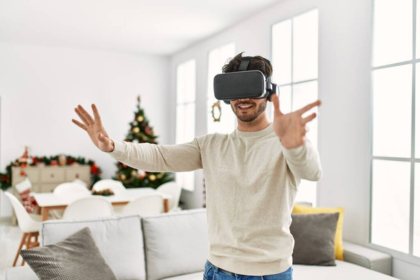 Junger hispanischer Mann lächelt glücklich mit 3D-VR-Brille zu Hause. - Foto, Bild