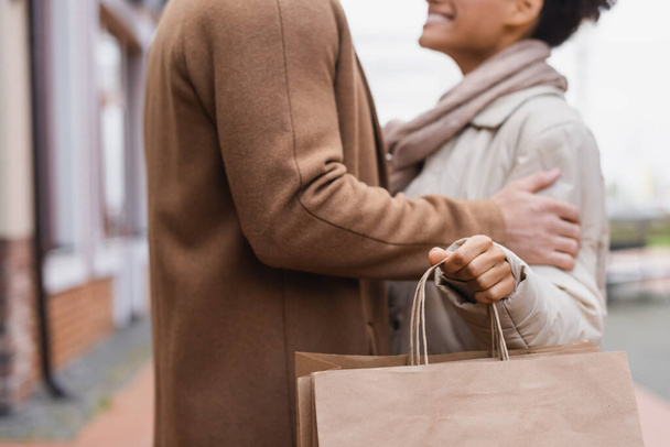 vista cortada de mulher americana africana alegre segurando sacos de compras perto de namorado ao ar livre  - Foto, Imagem