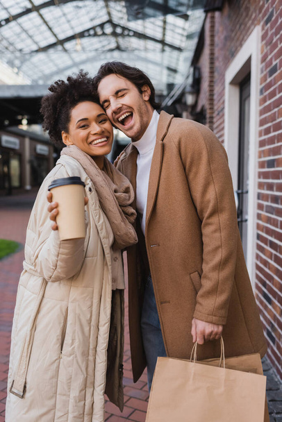 happy african american woman holding  paper cup with coffee to go near excited boyfriend with purchases  - Photo, Image