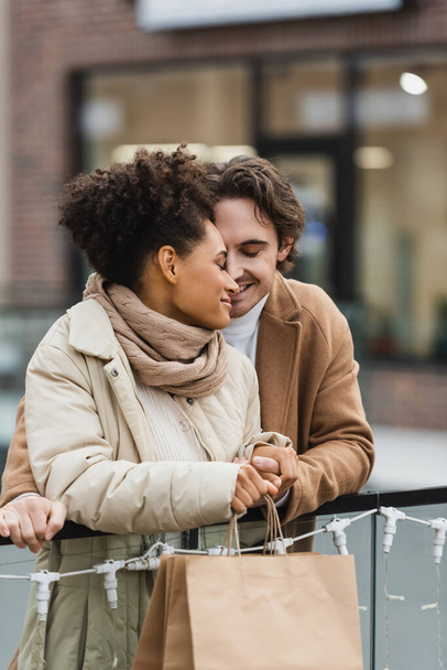 homme heureux tenant la main avec souriant afro-américaine petite amie dans le centre commercial  - Photo, image