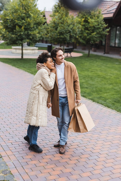 happy african american woman embracing cheerful boyfriend with shopping bags outside  - Foto, Imagem