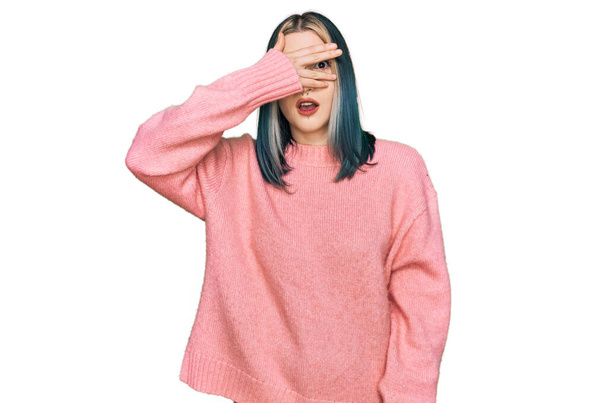 Giovane ragazza moderna che indossa maglione invernale di lana rosa sbirciare in shock che copre il viso e gli occhi con la mano, guardando attraverso le dita con espressione imbarazzata.  - Foto, immagini
