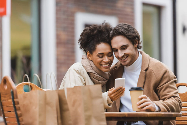 happy african american woman holding smartphone near boyfriend with paper cup  - Photo, Image