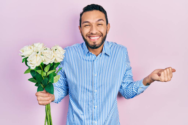 Hispánec s vousy drží kytice bílých květin křičí hrdě, slaví vítězství a úspěch velmi vzrušený s zvednutou paží  - Fotografie, Obrázek