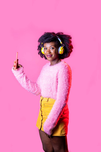 Young black woman holding smartphone videocalling wearing wireless headphones isolated background - Valokuva, kuva