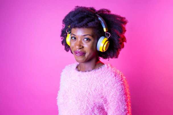 Portret jonge zwarte vrouw kijken over luisteren muziek draadloze hoofdtelefoon glimlachen gelukkig en serene geïsoleerde achtergrond - Foto, afbeelding