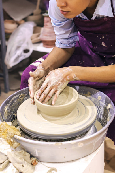 Vrouw keramische kunstenaar gieten klei op aardewerk wiel bij kunst workshop.  - Foto, afbeelding