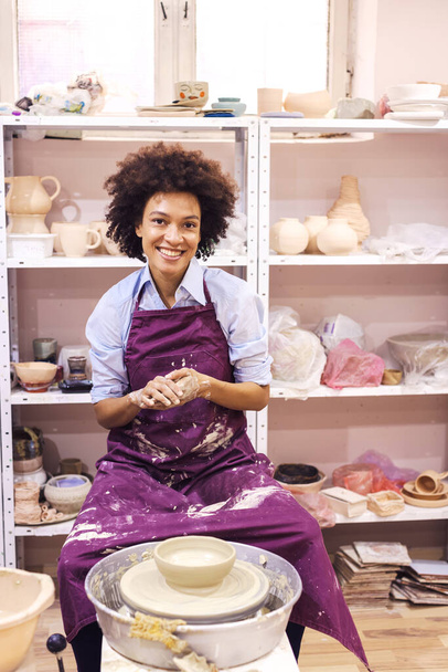 Творча афро-американська молода жінка, що формує глину на керамічному колесі. Фабрика в керамічній студії.. - Фото, зображення