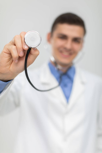 The doctor picks up his stethoscope and positions it directly to the camera. He smiles. - 写真・画像