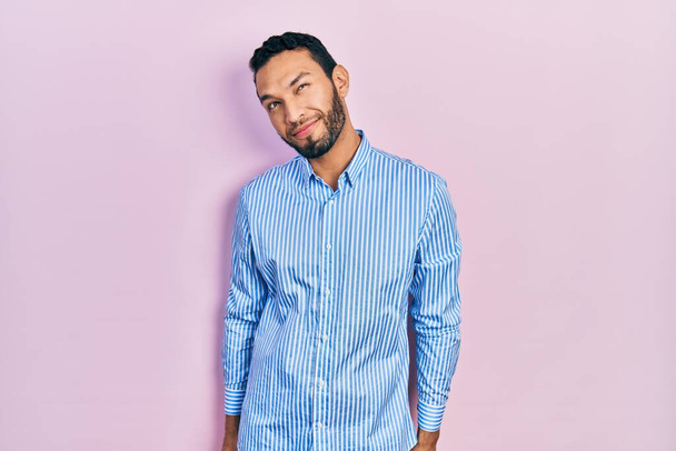 Spaanse man met baard in casual blauw shirt glimlachend naar de zijkant kijkend en wegkijkend denkend.  - Foto, afbeelding