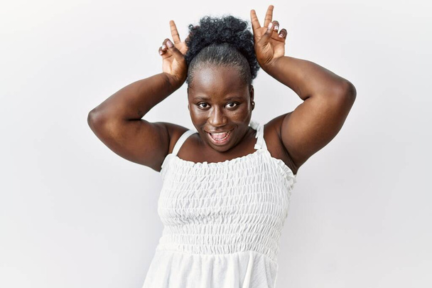 Young african woman standing over white isolated background posing funny and crazy with fingers on head as bunny ears, smiling cheerful  - Foto, Imagen