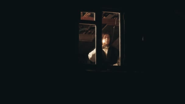 Vrouw op zolder van huis. Ze geeft signaal met kaars uit het raam. - Video