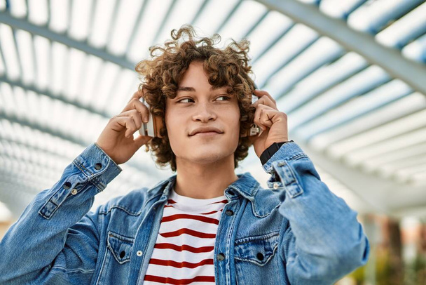 Young hispanic man listening to music wearing headphones at the city - Zdjęcie, obraz