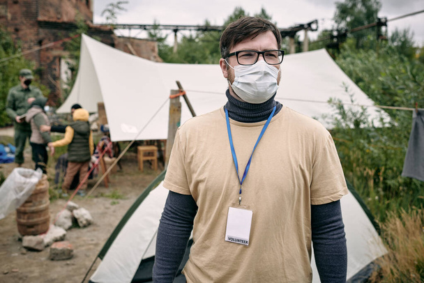 Молодий волонтер у захисній масці, що стоїть у таборі біженців
 - Фото, зображення