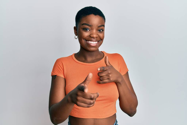 Fiatal afro-amerikai nő alkalmi narancssárga pólóban, ujjal mutogatva a kamerára, boldog és vicces arccal. jó energia és rezgések.  - Fotó, kép