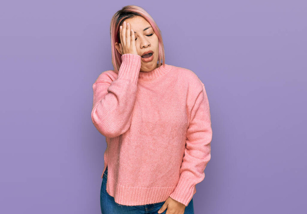 Spaanse vrouw met roze haar draagt casual winter trui geeuwen moe bedekken half gezicht, oog en mond met de hand. gezicht doet pijn in pijn.  - Foto, afbeelding