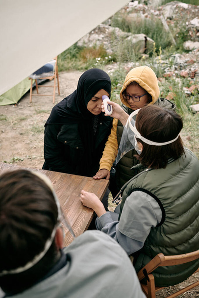 Ehrenamtliche Ärztin misst Körpertemperatur junger Flüchtlingsfrauen - Foto, Bild